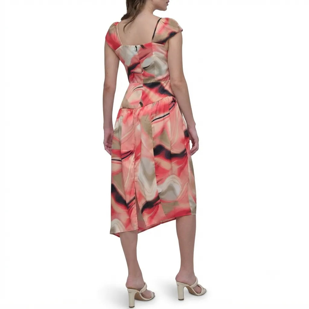 A woman modeling a sleeveless midi dress from the back, featuring a draped, wrap-style bodice and an abstract watercolor print in coral pink, beige, and black, set against a plain white background.
