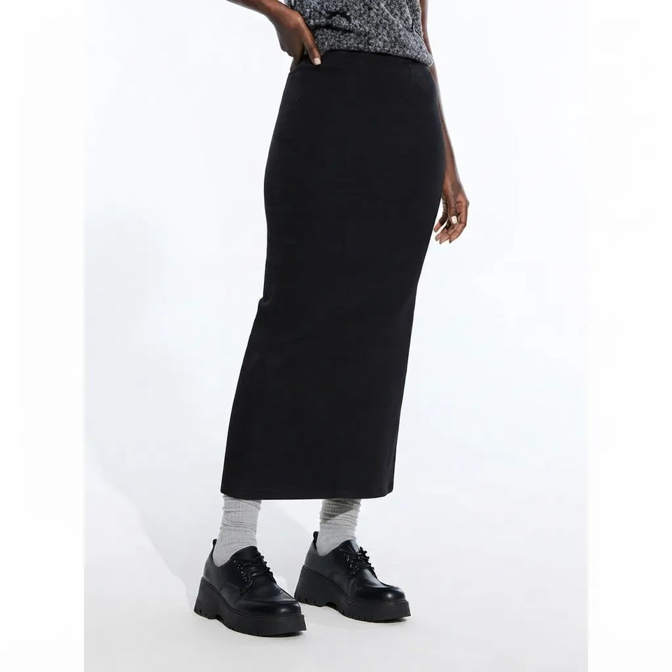A model wearing a black midi-length pencil skirt, paired with gray socks and black platform lace-up shoes, shown against a plain white studio background.