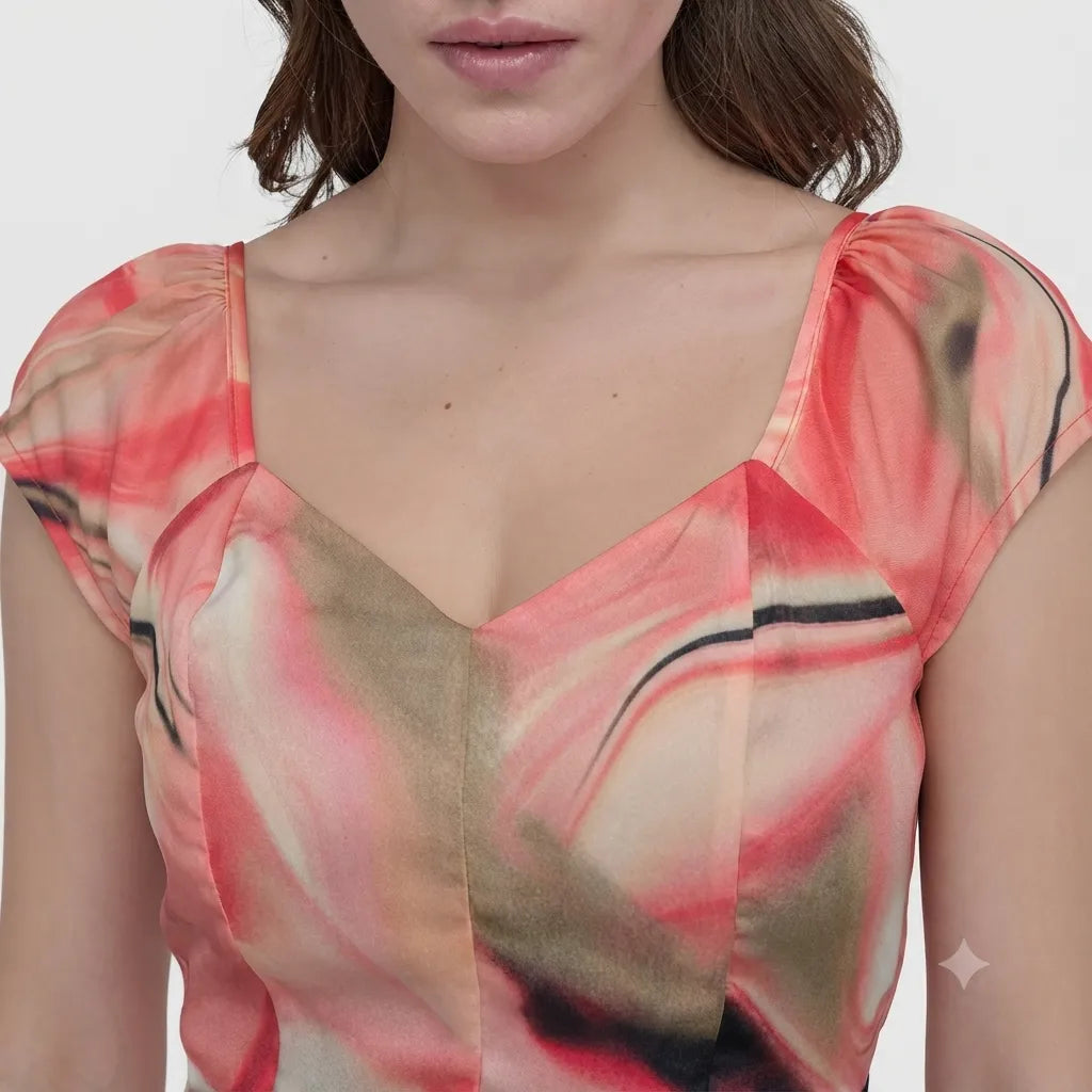 A close-up of a woman wearing a sheer puff-sleeve top with an abstract print in coral pink, beige, and black on a light gray background.
