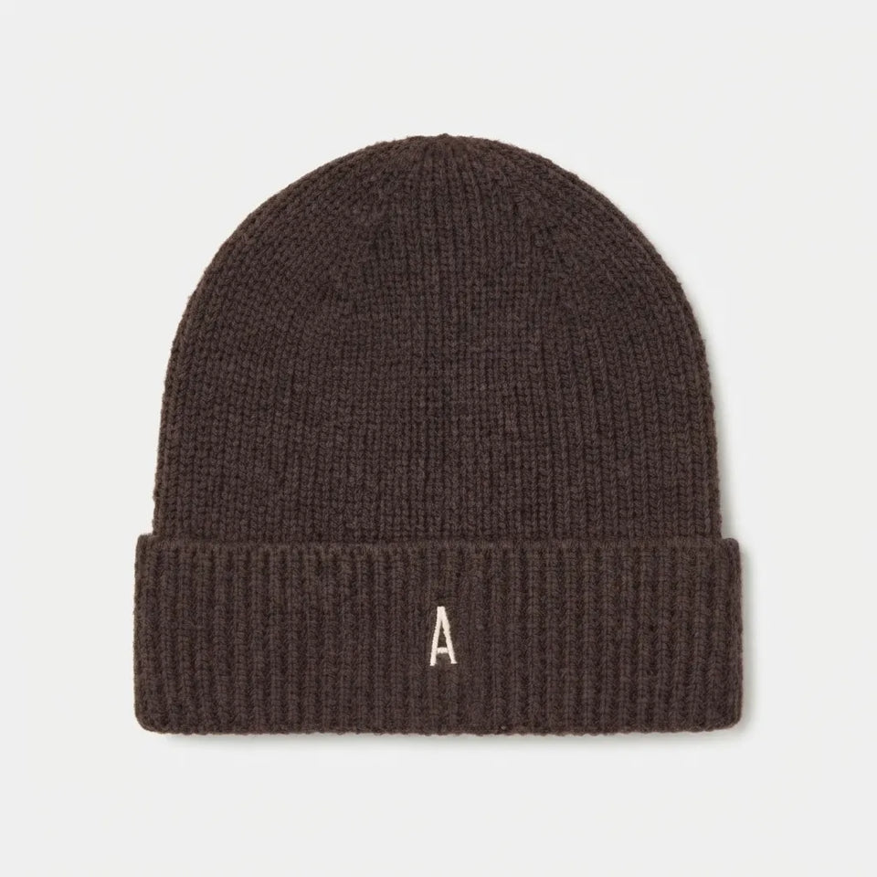 A dark brown ribbed knit beanie hat featuring a small white embroidered letter 'A' on the front of the folded cuff, shown against a light gray background.