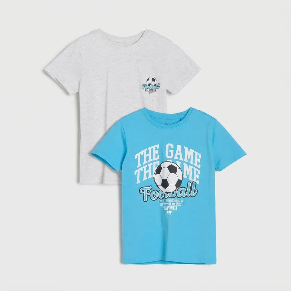 Two kids' short-sleeve t-shirts displayed on a light gray background. The front shirt is bright light blue with a white and black soccer graphic and the text 'THE GAME THE GAME Football'.