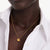 A close-up of a model wearing a delicate gold chain necklace with a small interlocking double-C pendant, styled with a white button-down shirt.