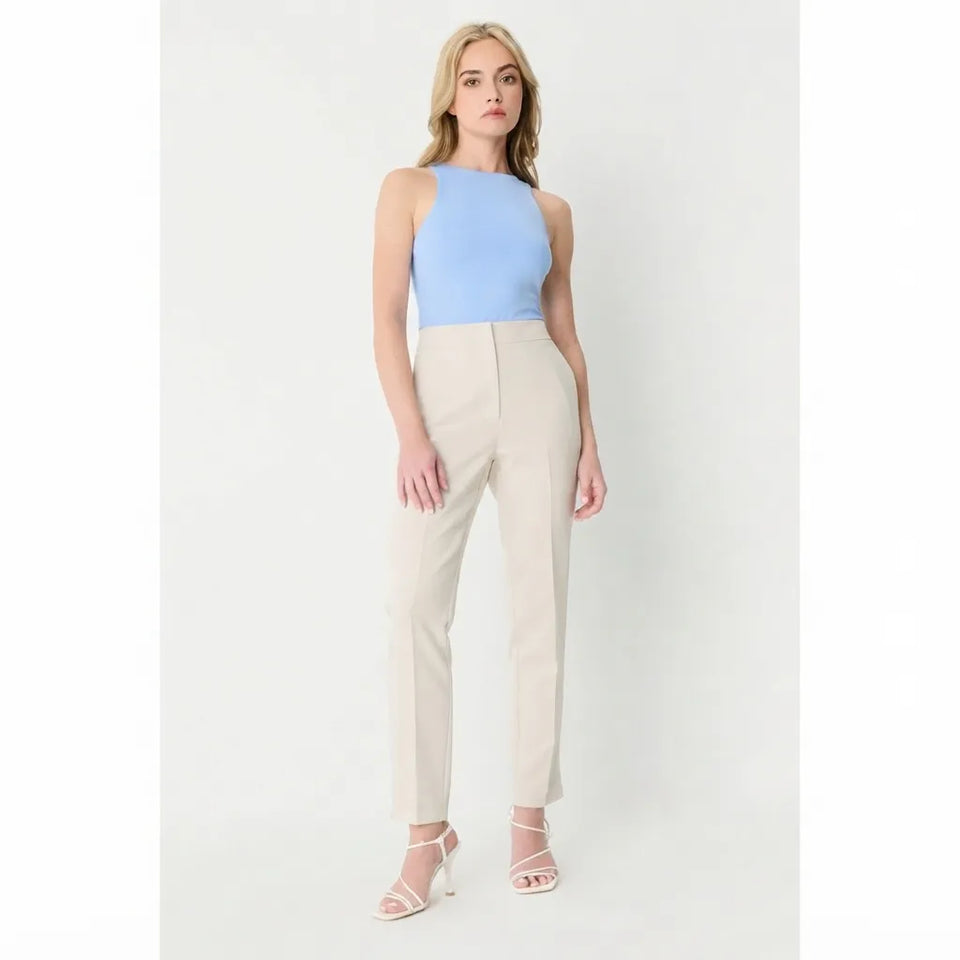 A woman modeling a sleeveless light blue top and beige straight-leg trousers with white strappy high-heeled sandals, standing against a plain light gray studio background.