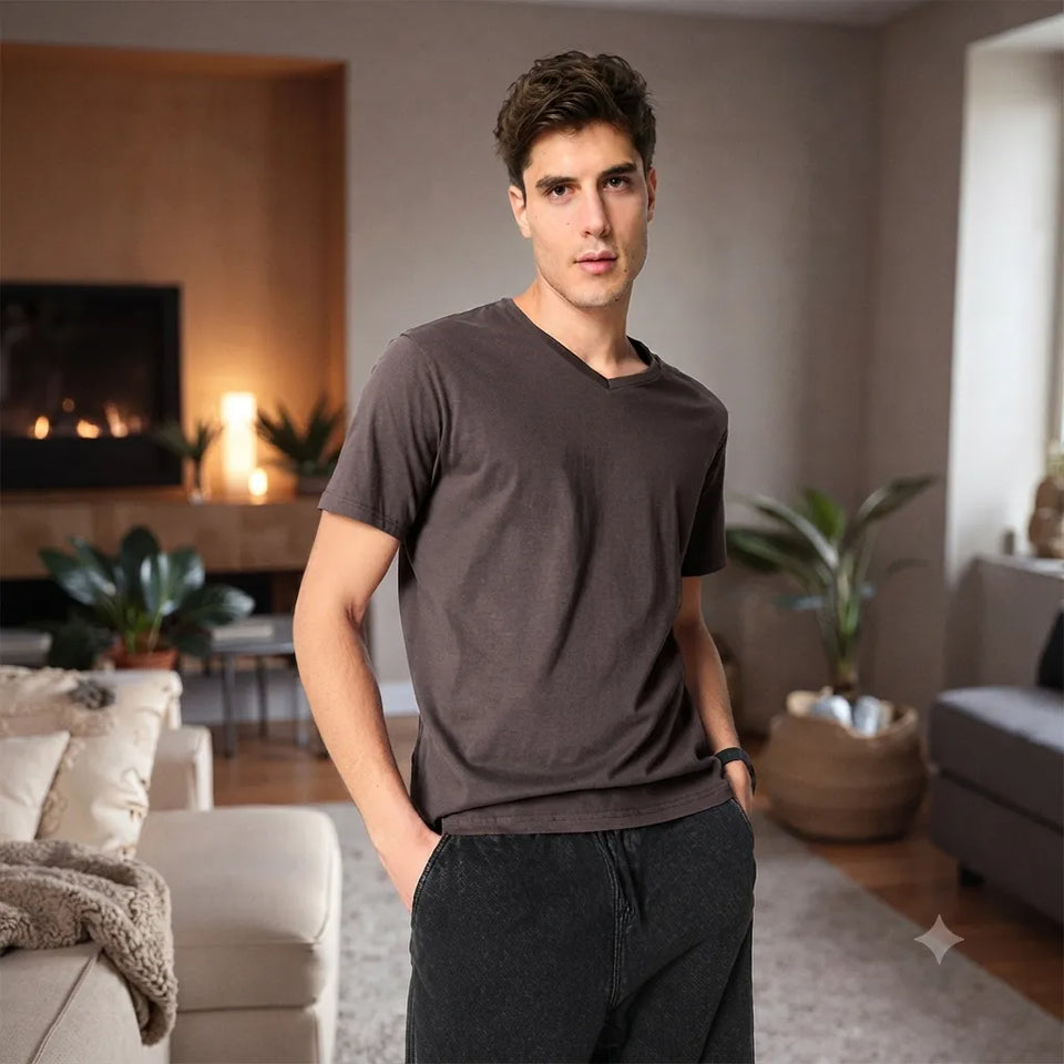A man wearing a dark brown v-neck t-shirt and dark gray sweatpants, standing in a modern living room with a fireplace in the background.