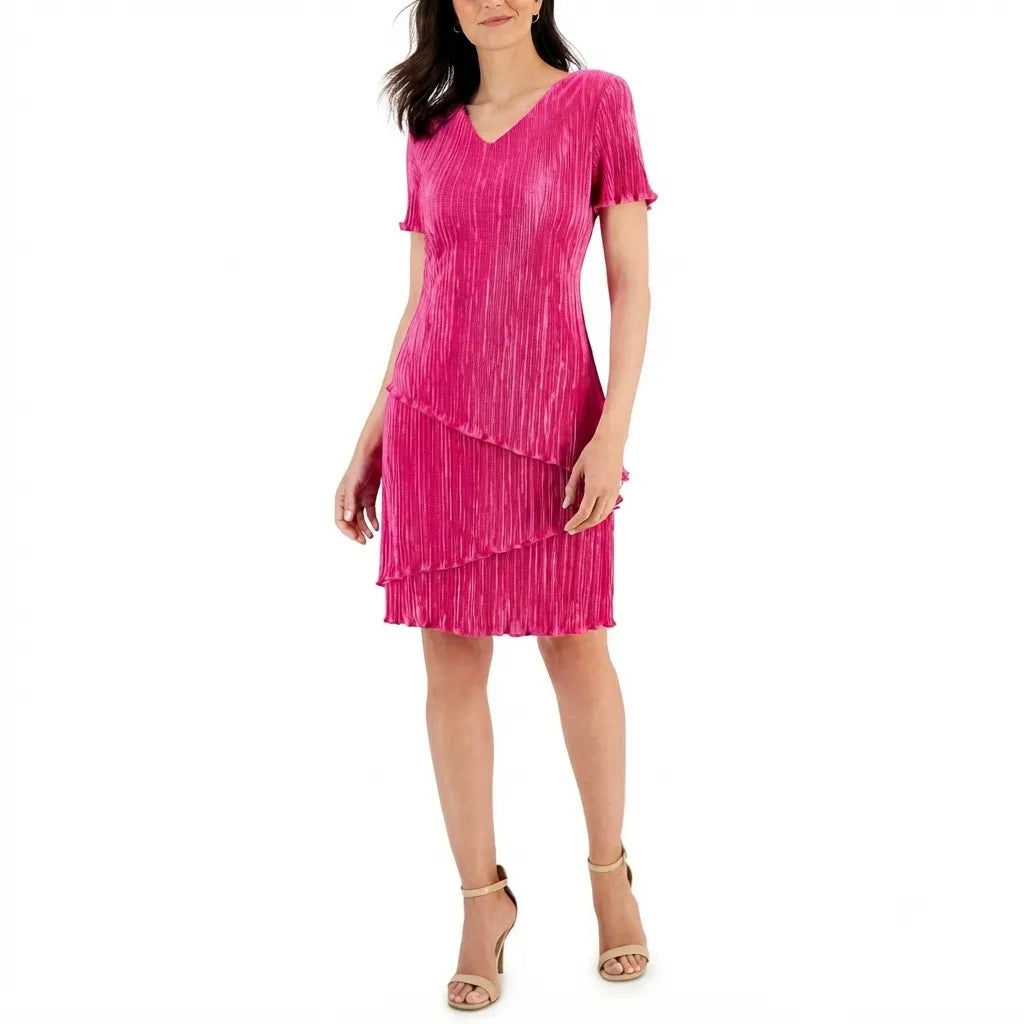 A woman modeling a bright pink pleated short-sleeve V-neck dress with a tiered skirt, paired with beige heeled sandals, against a plain white background.
