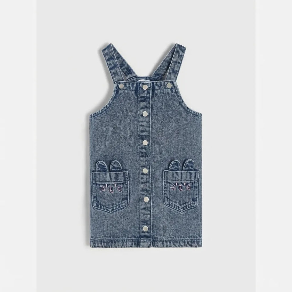 A toddler's denim overall-style top with adjustable shoulder straps, a snap-button front, and two front patch pockets, shown flat against a light gray background.