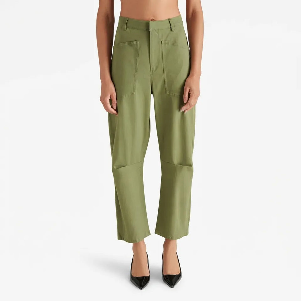A model is shown from the waist down wearing olive green cropped trousers with front patch pockets and black pointed-toe heels, set against a plain white studio background.