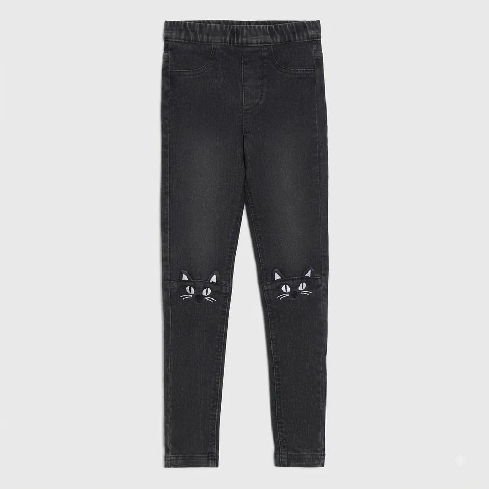 Black denim leggings with embroidered cat face details on the lower legs, shown flat against a light gray background.
