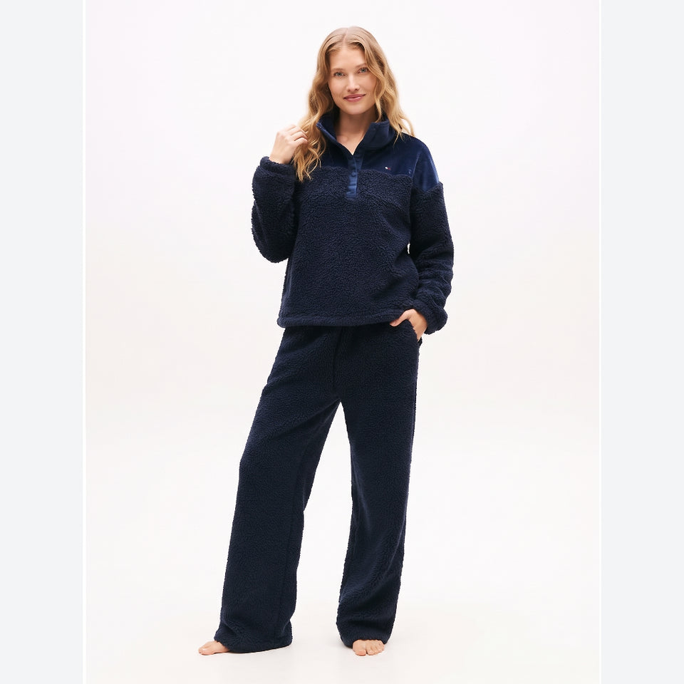 A woman modeling a matching navy blue fleece pajama set, consisting of a quarter-zip pullover and wide-leg pants, against a plain white studio background.