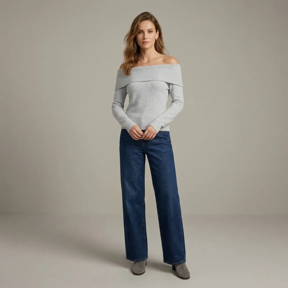 A woman modeling an off-the-shoulder light gray knit sweater and dark blue wide-leg jeans against a neutral studio backdrop.