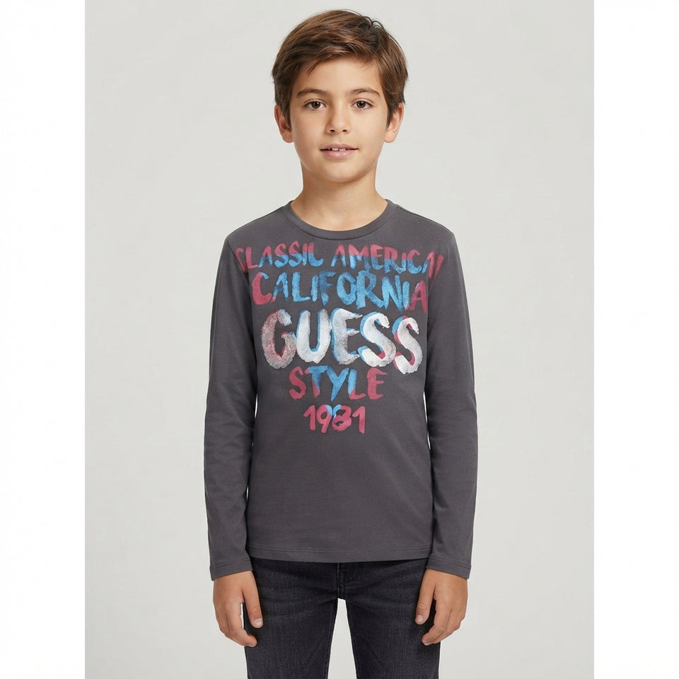 A young boy modeling a dark gray long-sleeve t-shirt with a colorful graphic print on the front that reads 'CLASSIC AMERICAN CALIFORNIA GUESS STYLE 1991'.