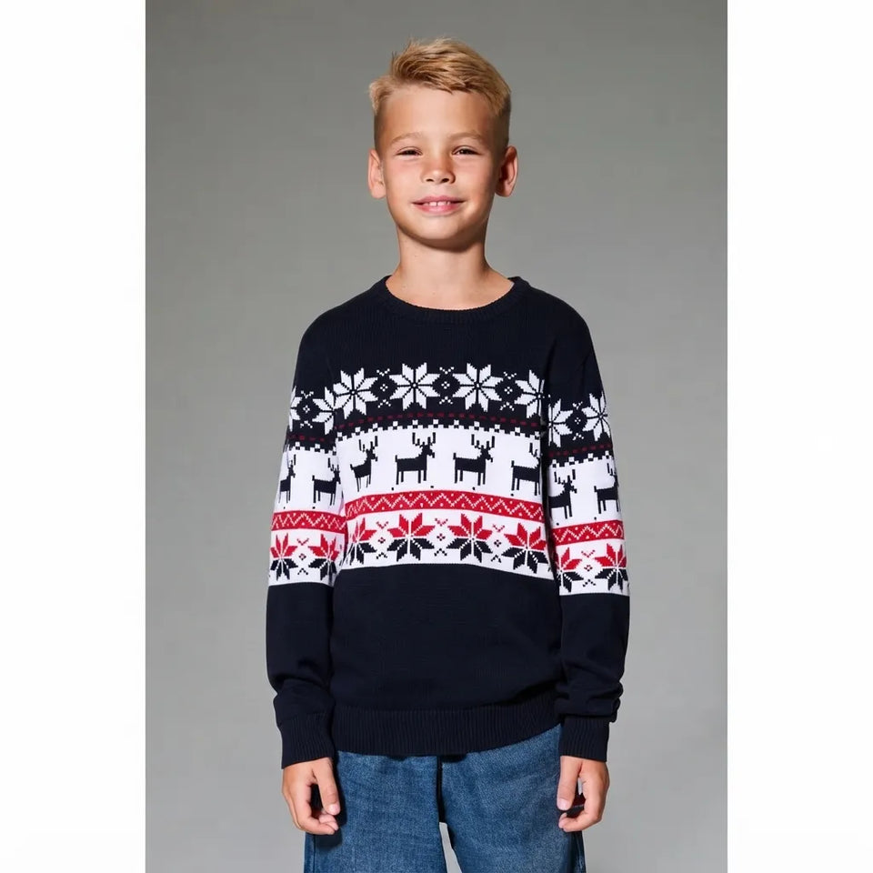 A young boy wearing a navy blue Christmas sweater with white and red holiday patterns, paired with blue jeans, standing against a solid gray background.