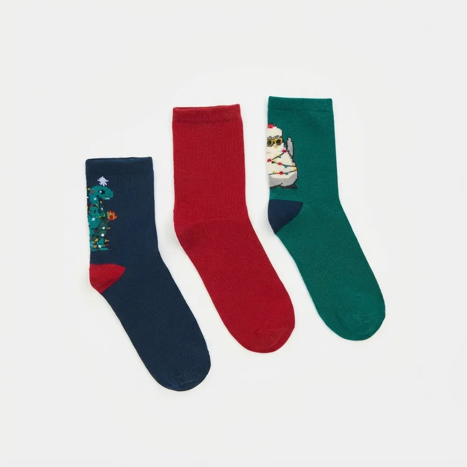 Three Christmas-themed crew socks laid flat on a white background: navy with a tree and lights, solid red, and green with a mummy and baby Jesus design.