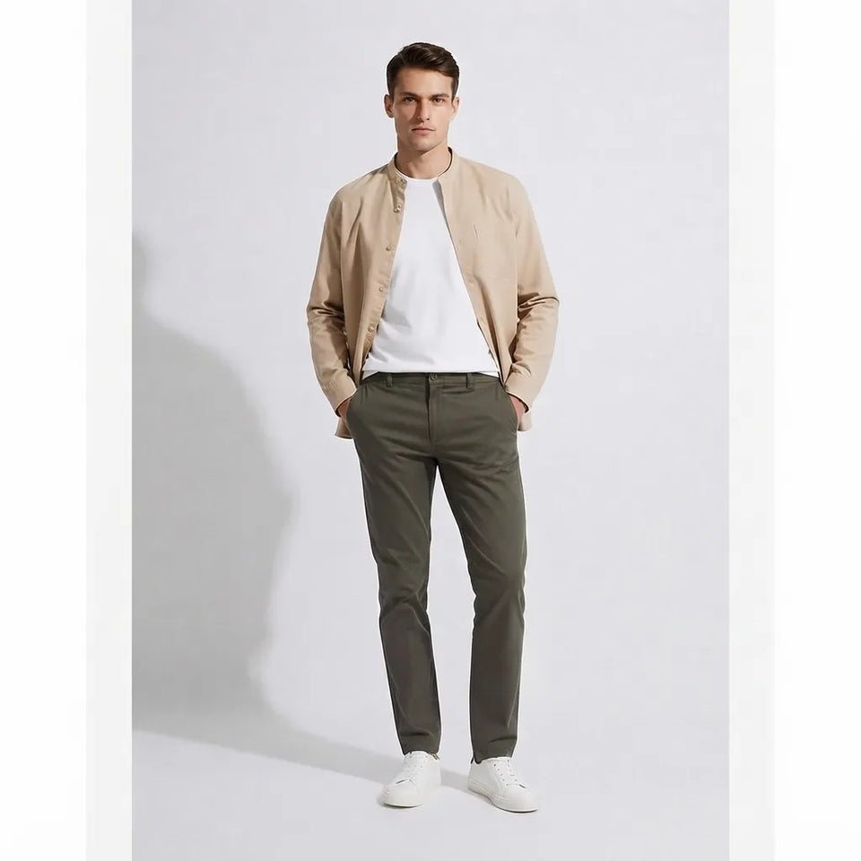 A man modeling a light beige bomber jacket over a white t-shirt, paired with olive green trousers and white sneakers, standing against a light gray studio background.