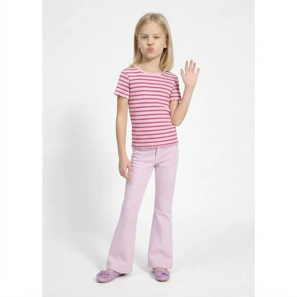 A young girl posing in a pink and white striped short-sleeve t-shirt, light pink flared pants, and matching pink shoes against a plain white studio background.