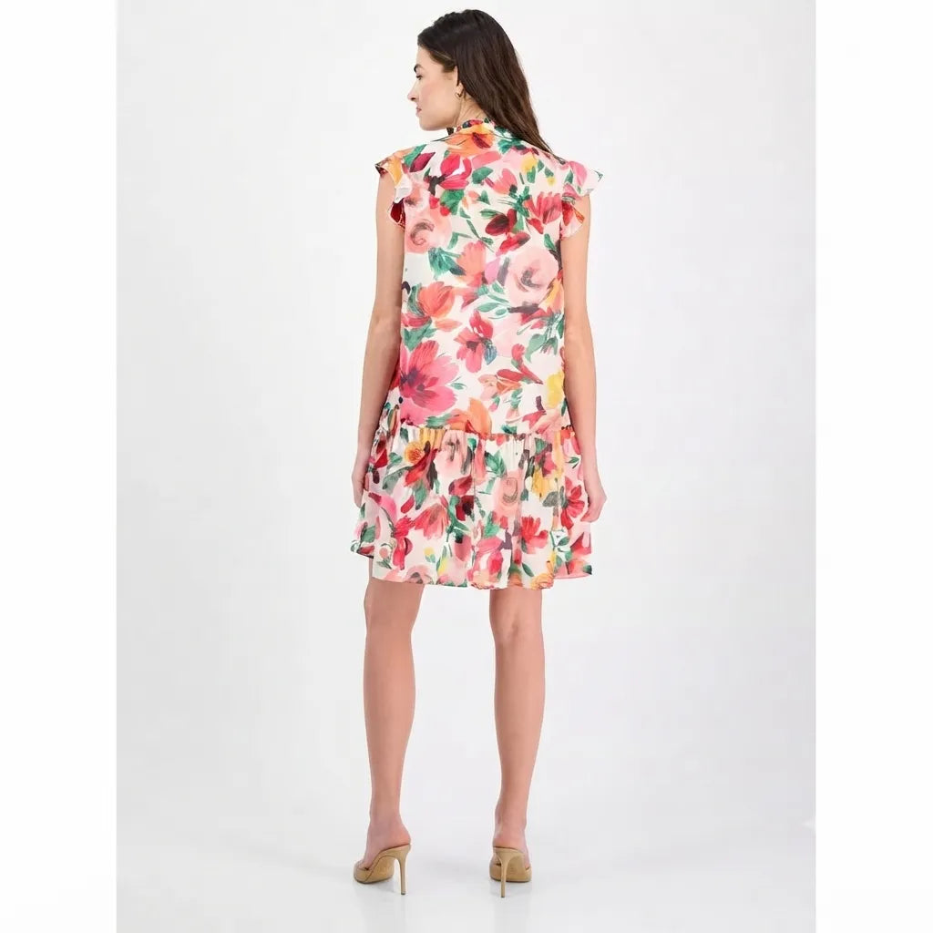 A woman modeling a sleeveless tiered shift dress with a vibrant multicolor floral print, shown from the back against a plain white studio background.
