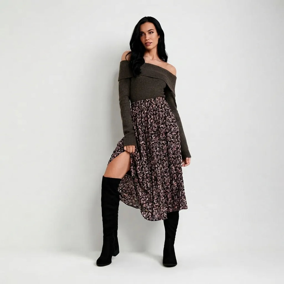 A woman models a dark olive green off-the-shoulder long-sleeve top paired with a dark floral print midi skirt and black over-the-knee boots, standing against a light gray studio background.