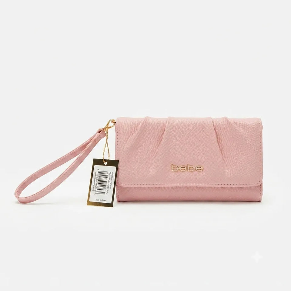 A light pink fabric wristlet clutch with gold-tone hardware, featuring a pleated front flap, a gold 'bebe' logo, and an attached product tag.