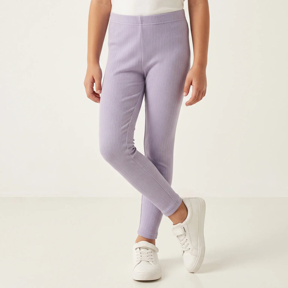 A child wearing light lavender ribbed leggings and white sneakers, standing against a clean off-white studio background.