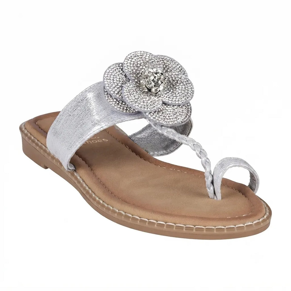A single women's thong sandal in metallic silver, featuring a wide textured strap, a braided toe loop, and a large rhinestone-embellished flower on the side, set against a plain white background.
