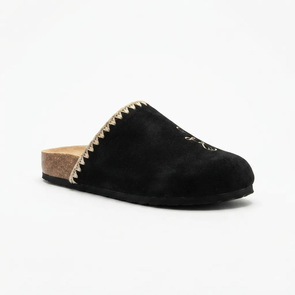 A black suede mule slipper with a pointed toe, a decorative zigzag trim of metallic gold and cream along the opening, and a natural cork heel, shown against a plain white background.