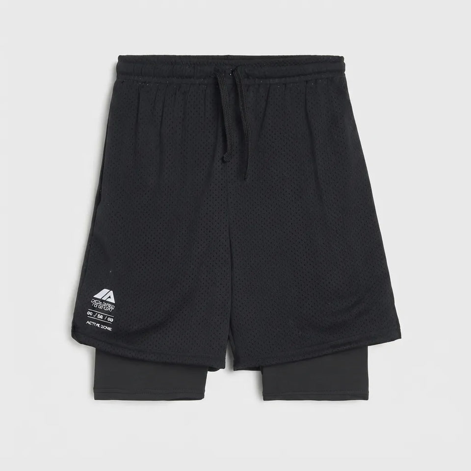 Black double-layered athletic shorts with a textured mesh outer layer, a black drawstring waist, and a white printed logo on the lower left leg, displayed against a light gray background.