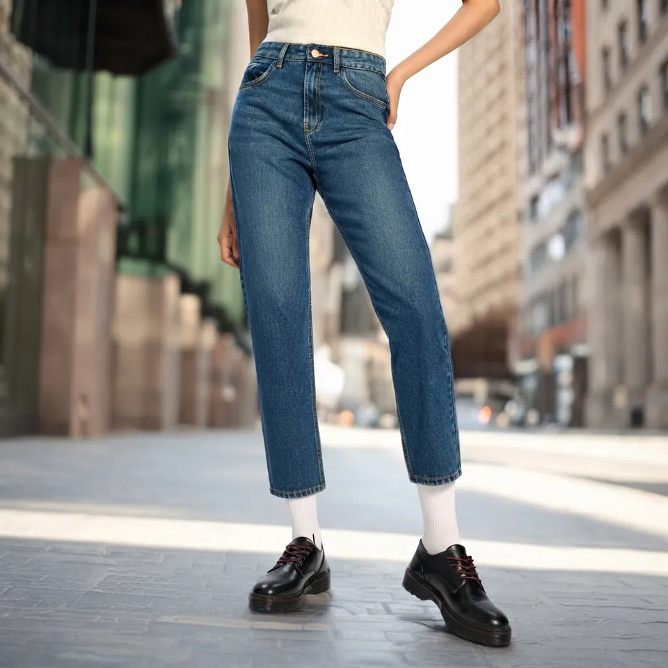 A person wearing blue straight-leg jeans, white socks, and black leather shoes standing on a city street.
