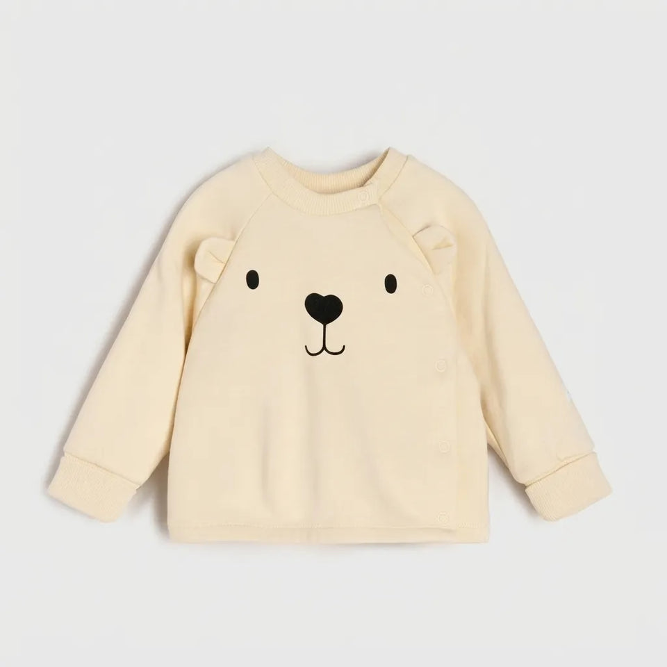 A cream-colored long-sleeve baby sweatshirt featuring a black embroidered bear face on the front, displayed against a light gray background.