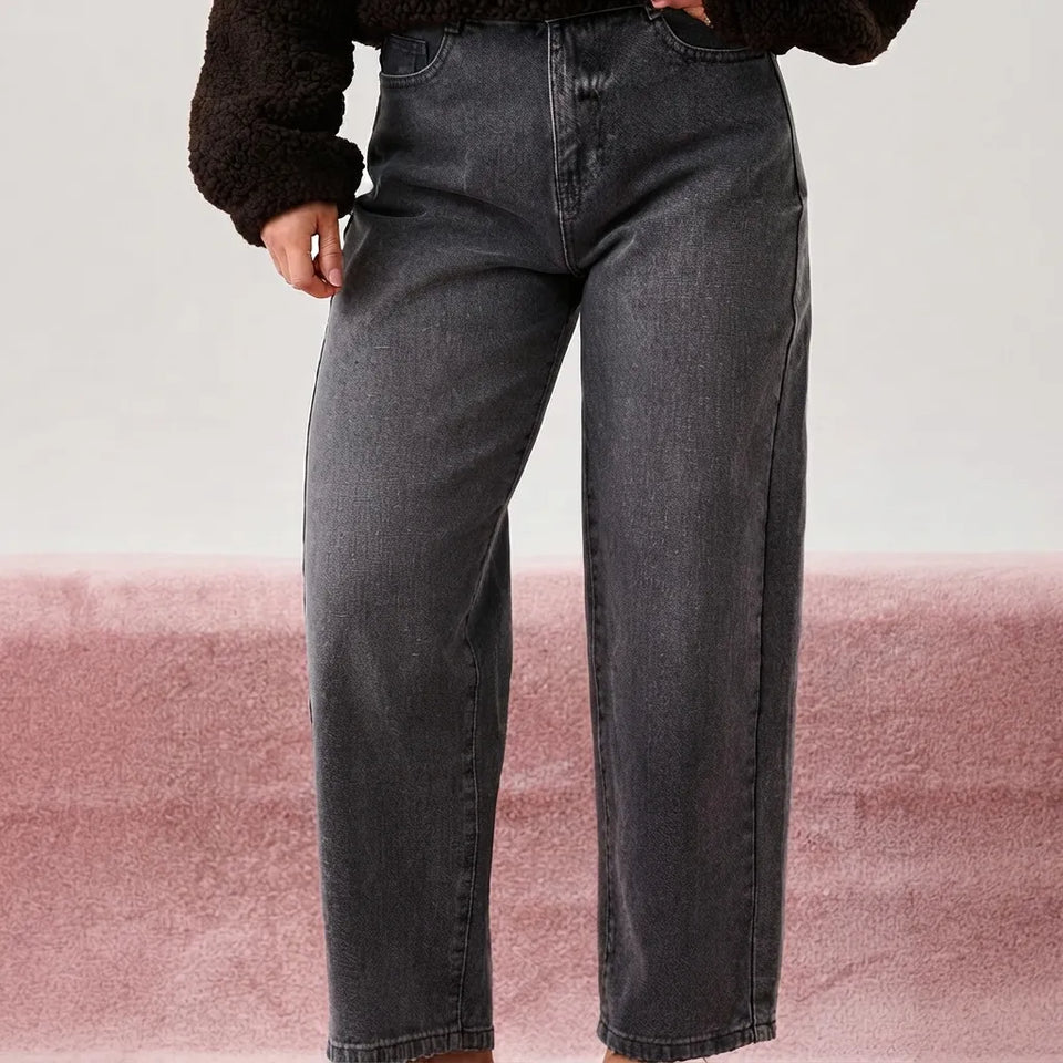 A person wearing dark gray wide-leg jeans and a dark brown fuzzy cropped sweater, standing against a split white and dusty pink background.