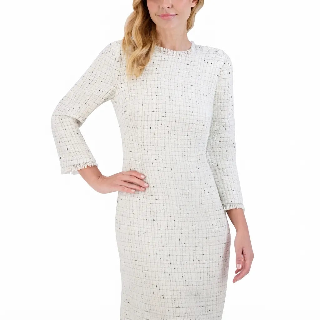 A woman wearing a cream-colored tweed dress with a subtle black grid pattern, featuring three-quarter sleeves with frayed cuffs, shown against a plain white background.