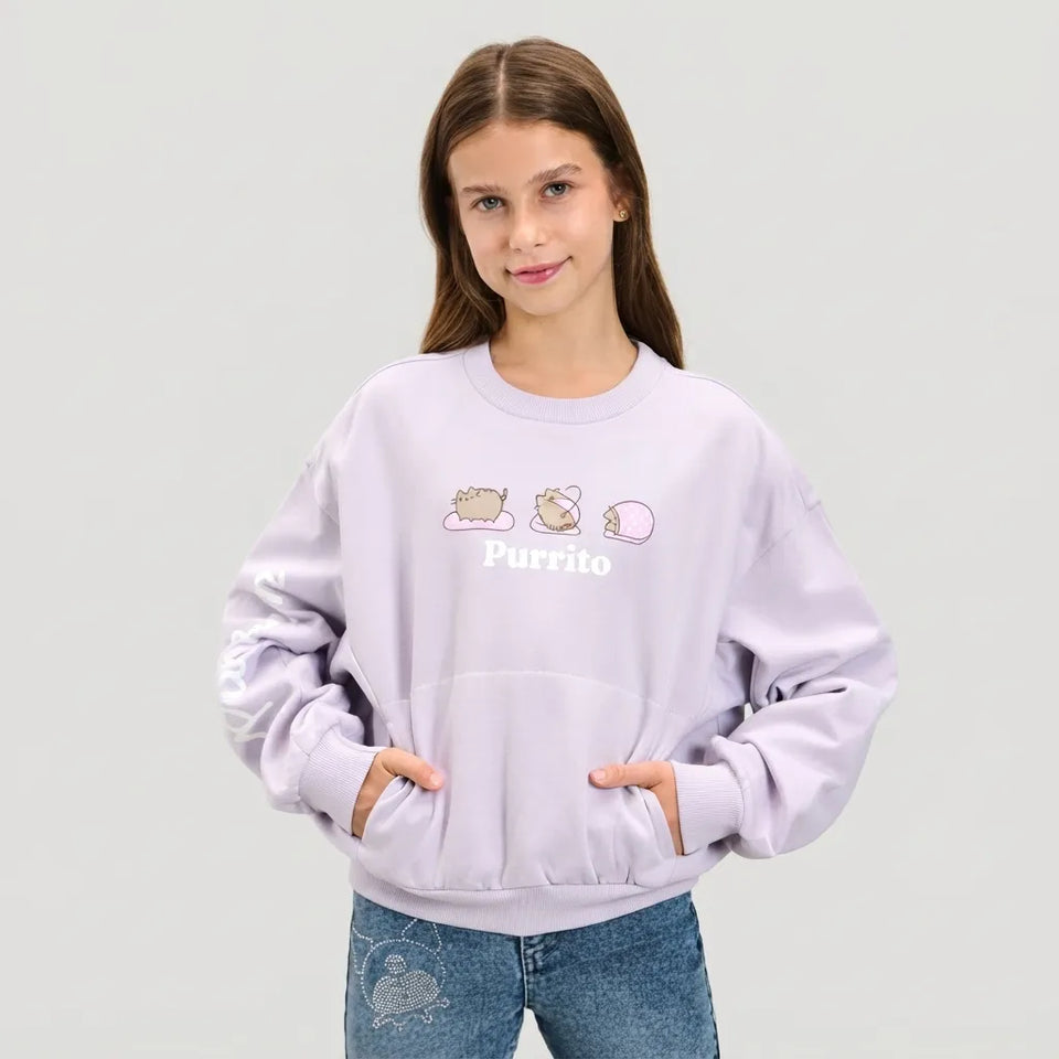 A young girl with long brown hair wearing a light lavender crewneck sweatshirt with a cute hamster graphic and the word 'Purrito' printed on the chest, paired with blue jeans, against a solid light gray background.