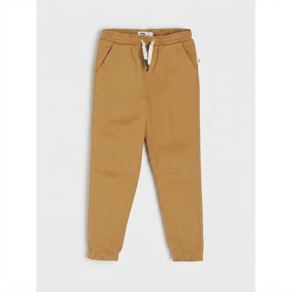 A pair of kids' jogger pants in a warm camel tan color, featuring an elastic waistband with a white drawstring and elastic cuffs, displayed flat against a light gray background.