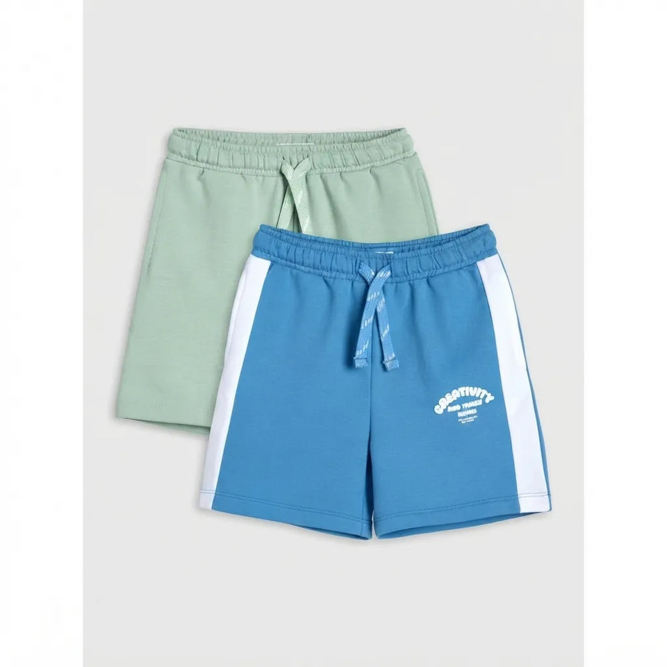 Two pairs of kids' athletic shorts, one in sage green and one in blue with white side stripes, displayed on a light gray background.
