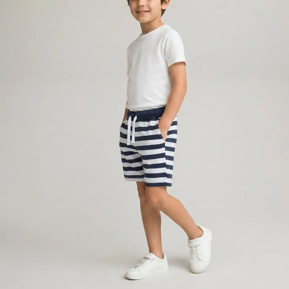 A child model wearing a white t-shirt, navy and white striped shorts, and white sneakers, standing against a light gray studio background.