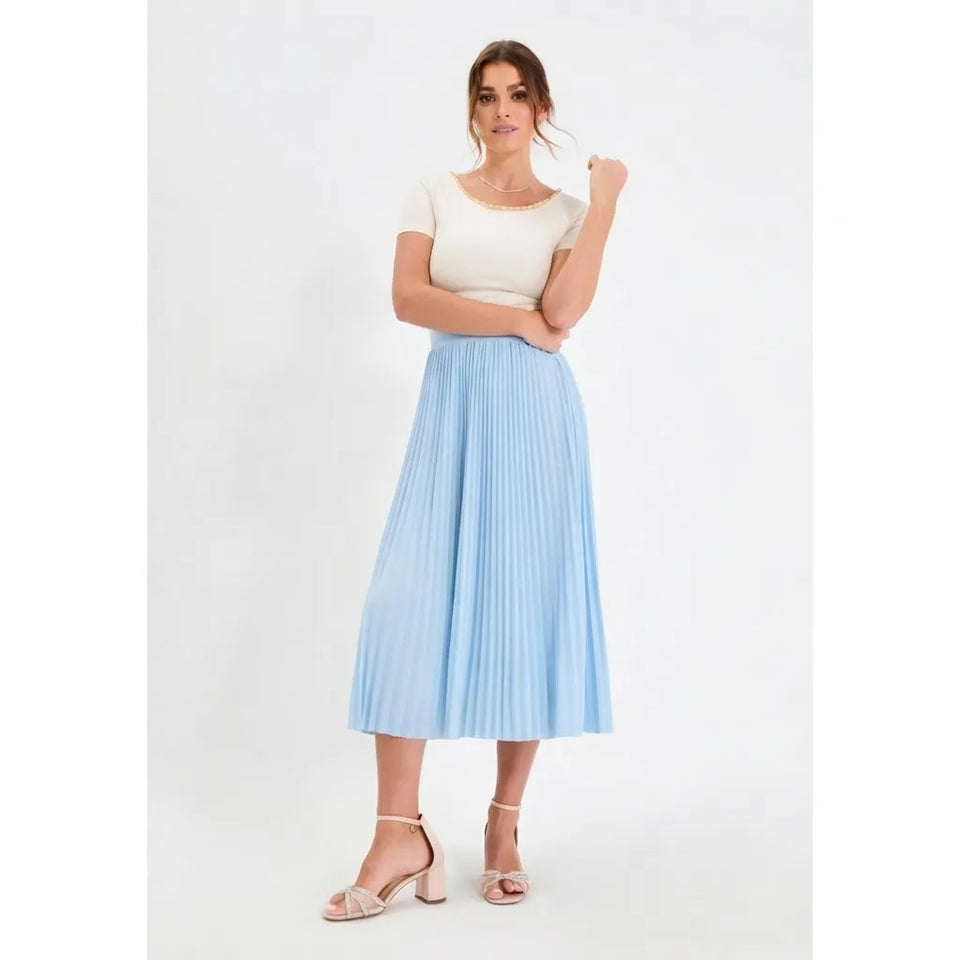 A woman modeling a light blue pleated midi skirt paired with a cream short-sleeve top and clear heeled sandals, standing against a plain white studio background.