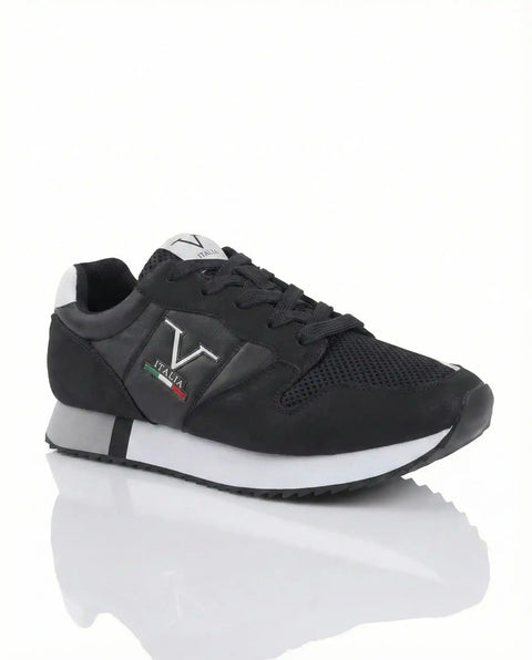 Black sneaker with white sole on a reflective white surface