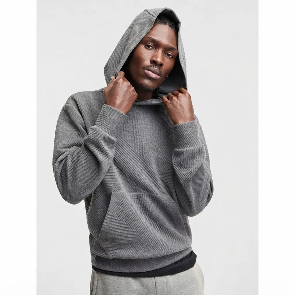 A man wearing a textured gray knit hoodie with a black ribbed hem, posing against a light gray background.