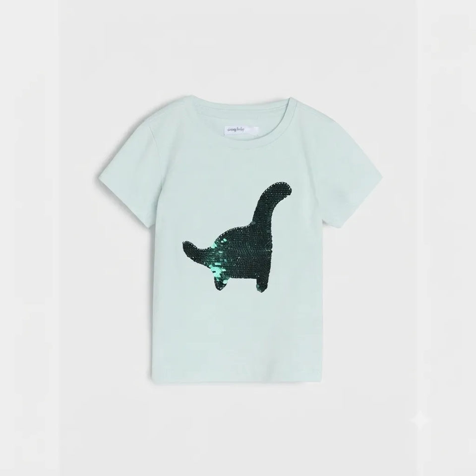 A light mint green short-sleeve t-shirt for kids, featuring a large black dinosaur silhouette printed on the front made of reversible sequins, set against a plain light gray background.