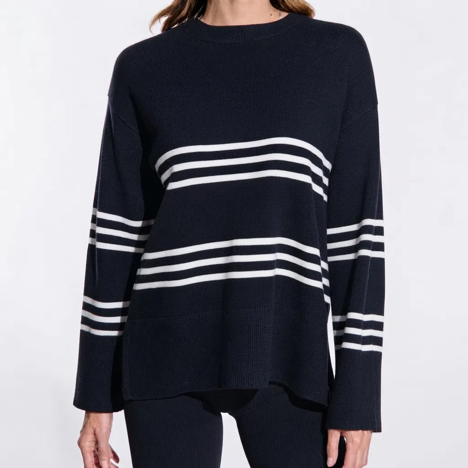 A woman wearing a navy blue knit sweater with horizontal white stripes across the chest and sleeves, shown against a plain light background.