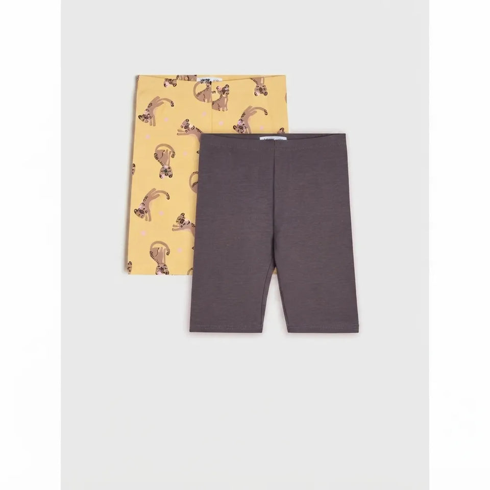 A pair of dark gray heathered bike shorts laid flat, with a matching pair of yellow leggings featuring a brown cat pattern tucked behind them on a light gray background.