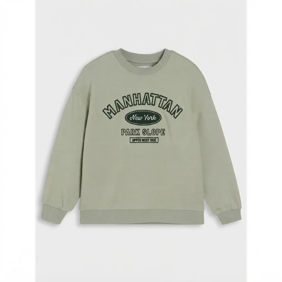 A sage green crewneck sweatshirt with a dark green graphic print on the front reading 'MANHATTAN New York PARK SLOPE EST. 2024', displayed against a light gray background.
