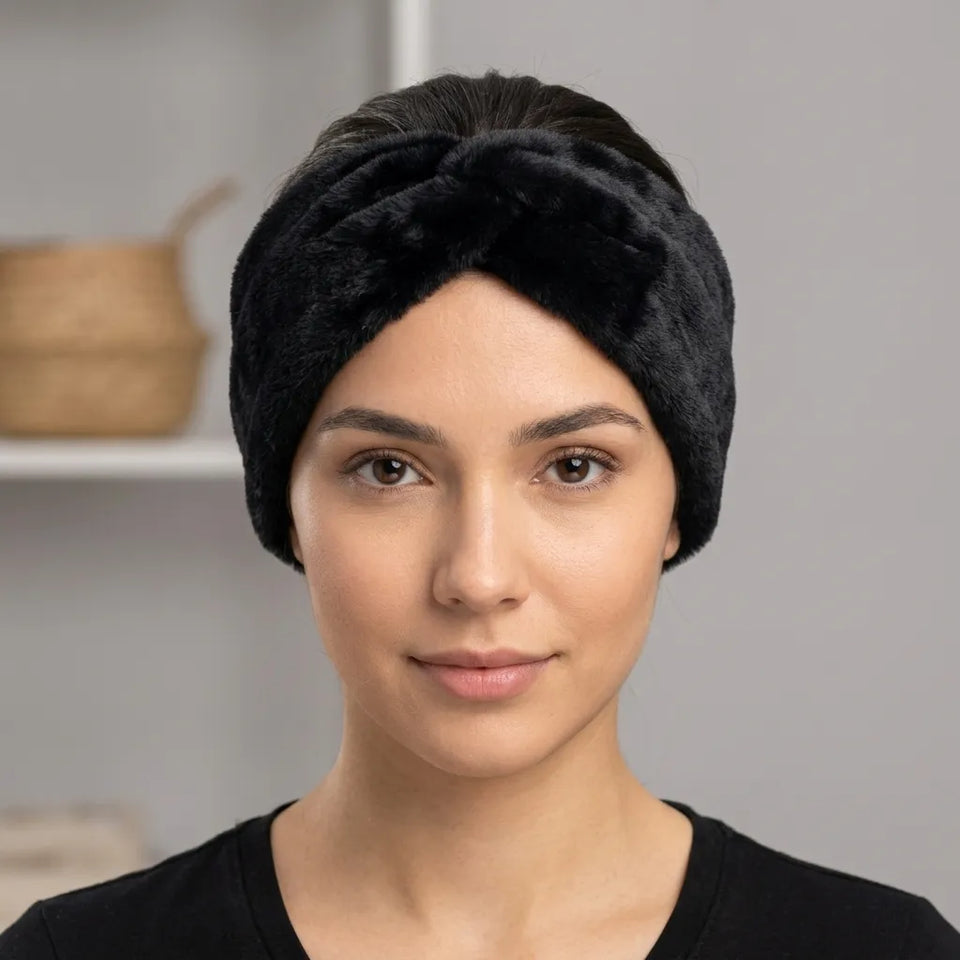 A woman wearing a black plush, textured headband with a knotted twist design, shown from the chest up against a soft gray background.