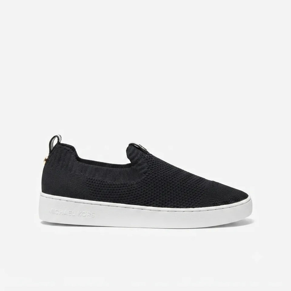 A black slip-on knit sneaker with a white sole, shown in profile against a light gray background. The brand name 'MICHAEL KORS' is debossed on the side of the white sole.