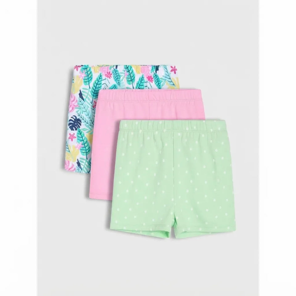 Three pairs of girls' shorts stacked together on a light gray background. The front pair is mint green with white polka dots, the middle pair is solid pink, and the back pair has a tropical leaf print with green, pink, yellow, and blue colors.