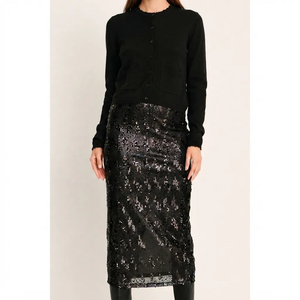 A model wearing a black long-sleeve button-front cardigan and a black sequined midi skirt, shown against a plain light beige studio background.