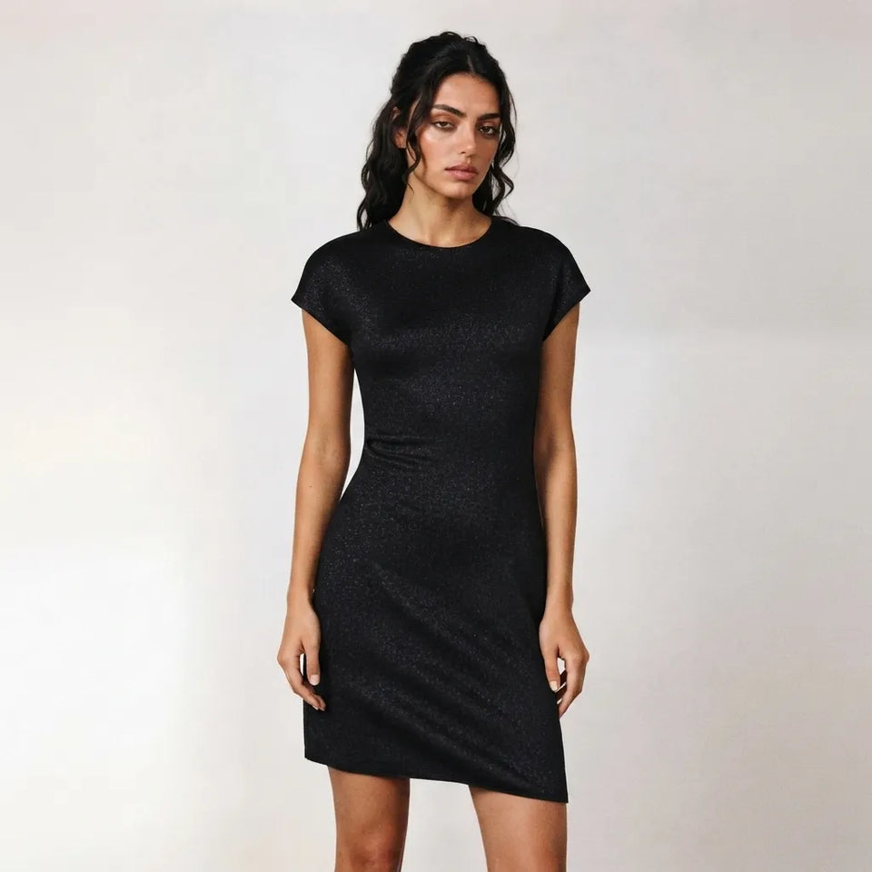 A woman modeling a short-sleeve black textured dress with a crew neck and side ruching, standing against a plain light gray studio background.