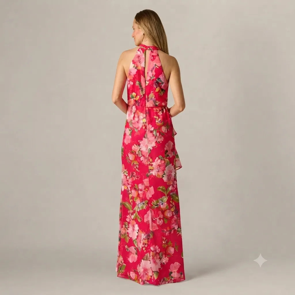 A woman wearing a sleeveless halter-neck maxi dress with a vibrant pink and red floral print, shown from the back against a neutral gray studio background.