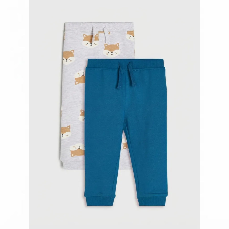 Two pairs of children's jogger pants laid flat on a light gray background. The front pair is solid teal blue with a drawstring waist, and the back pair is light gray with a repeating fox print in tan and cream.