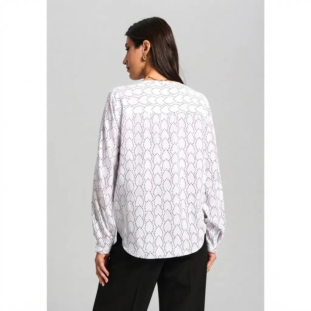 A woman shown from the back wearing a white long-sleeve blouse with a black geometric pattern, paired with black pants, against a solid gray studio background.