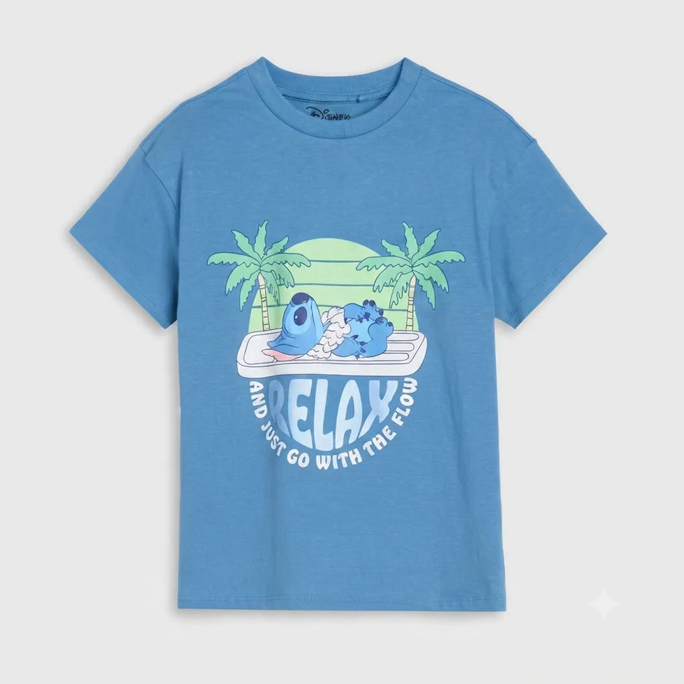 A heather blue short-sleeve t-shirt with a cartoon graphic of two blue characters relaxing on a surfboard between palm trees, with the text 'RELAX AND JUST GO WITH THE FLOW' printed below.